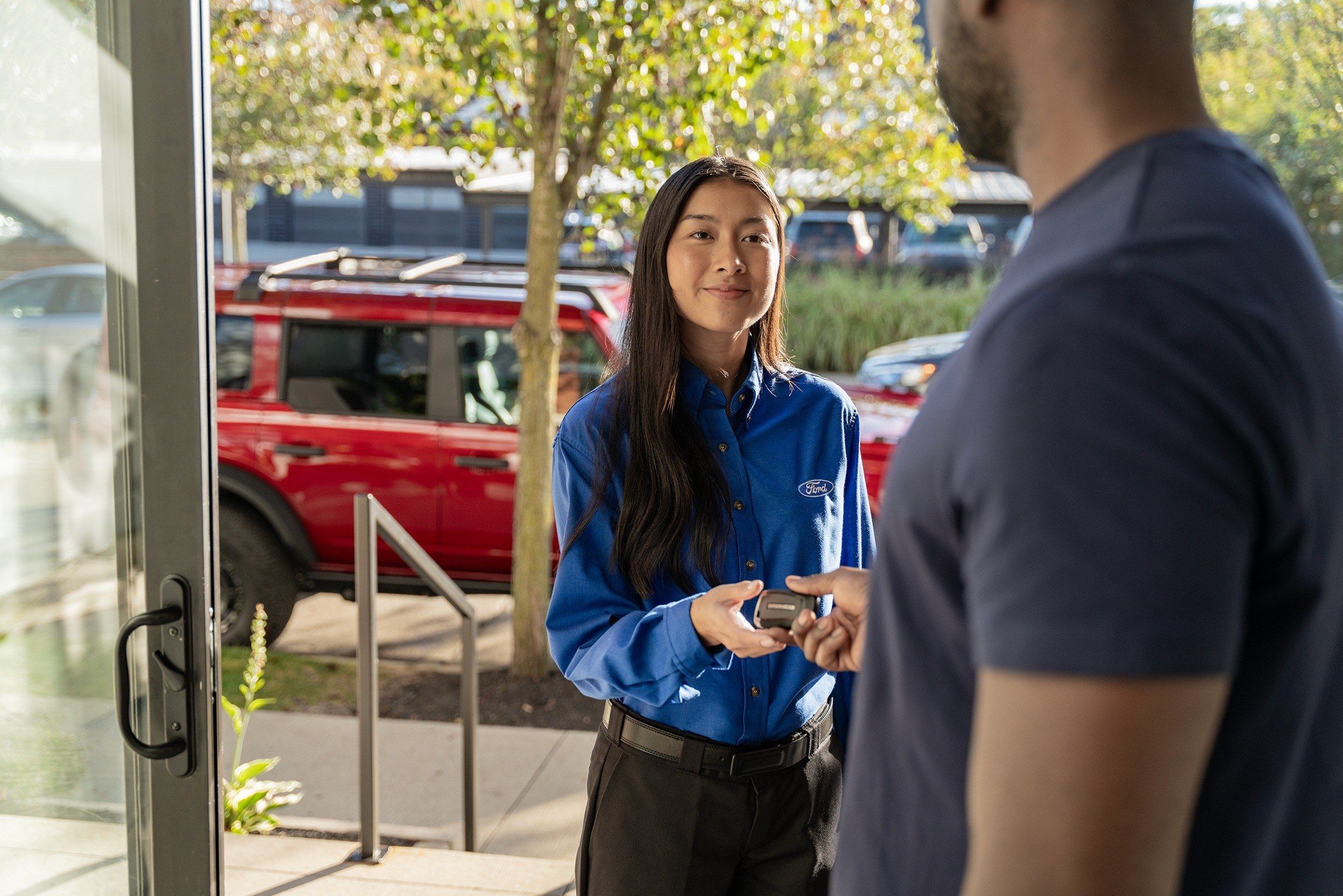 Smiling Ford service advisor handing car keys back to a customer at the dealership entrance