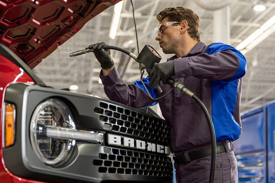 Ford technician working with an air hose at the front of a red Ford Bronco with the hood open