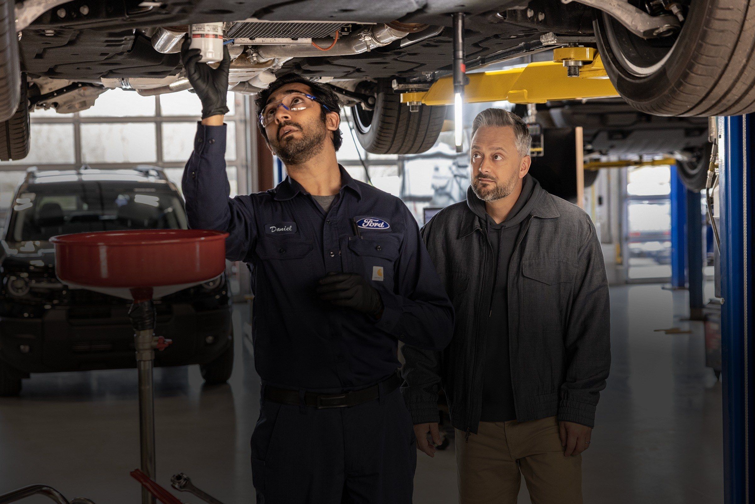 Ford technician showing a customer the underside of a vehicle raised on a lift