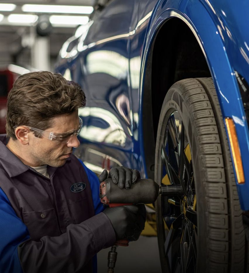 Ford technician using an impact wrench to mount a tire on a blue Ford vehicle