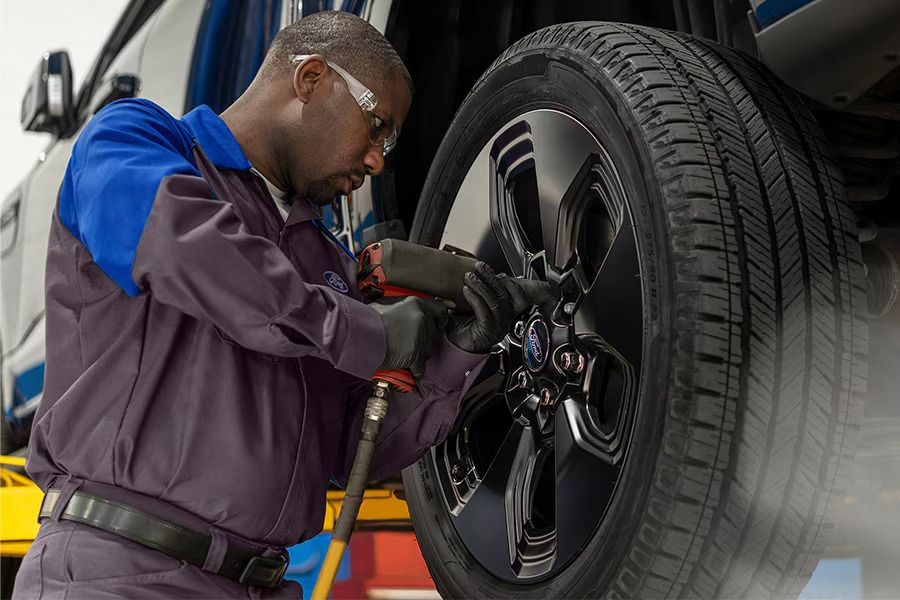 Ford technician in safety glasses using an impact wrench on the wheel lug nuts of a white Ford truck