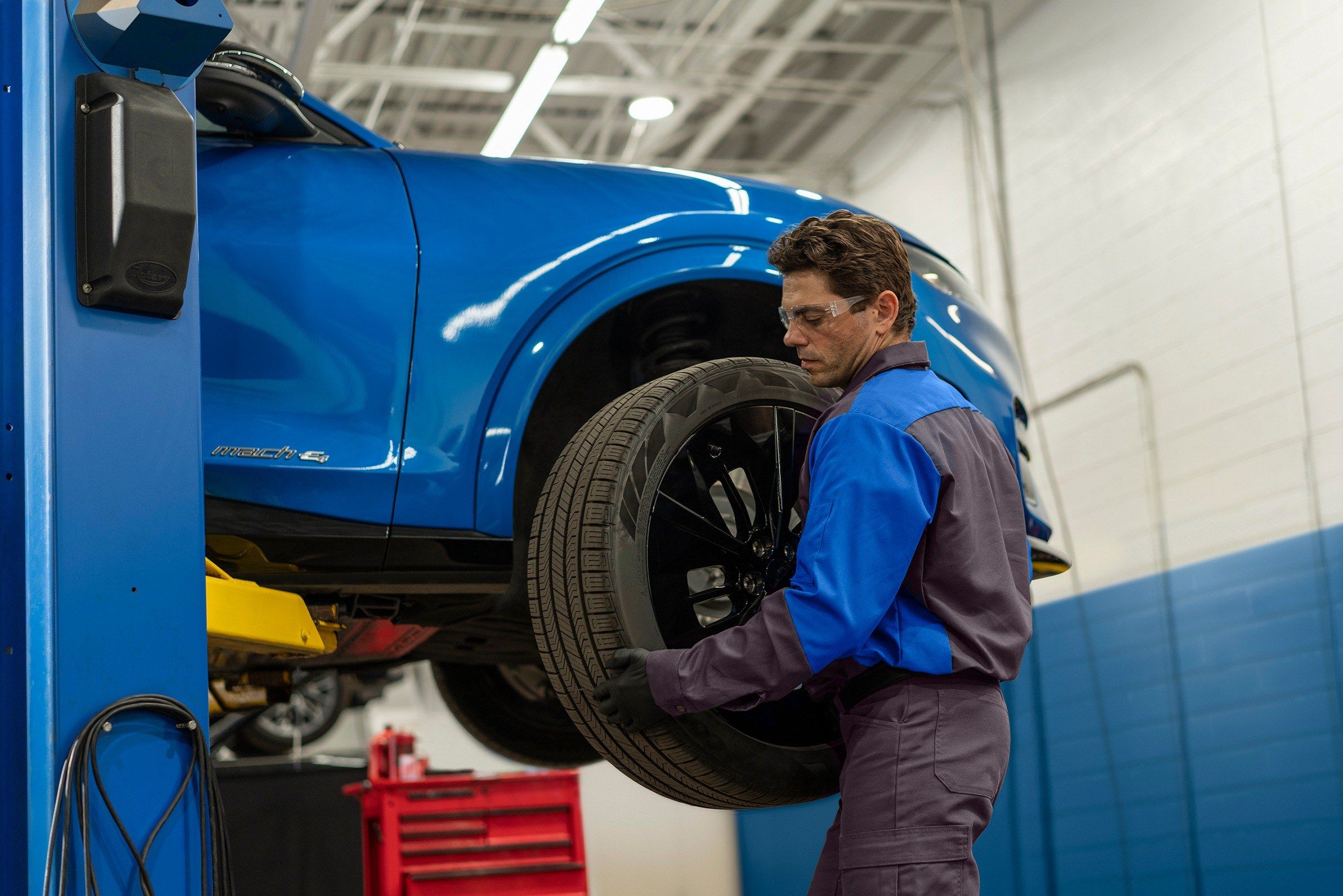 Ford technician fitting a tire on a blue Ford SUV raised on a lift